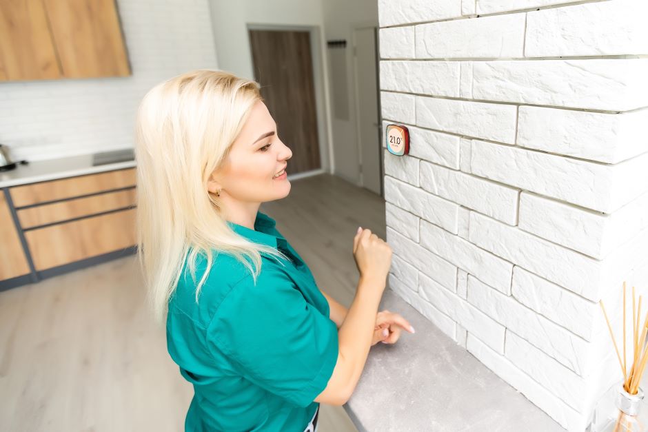 Blonde woman checking her home thermostat in kitchen