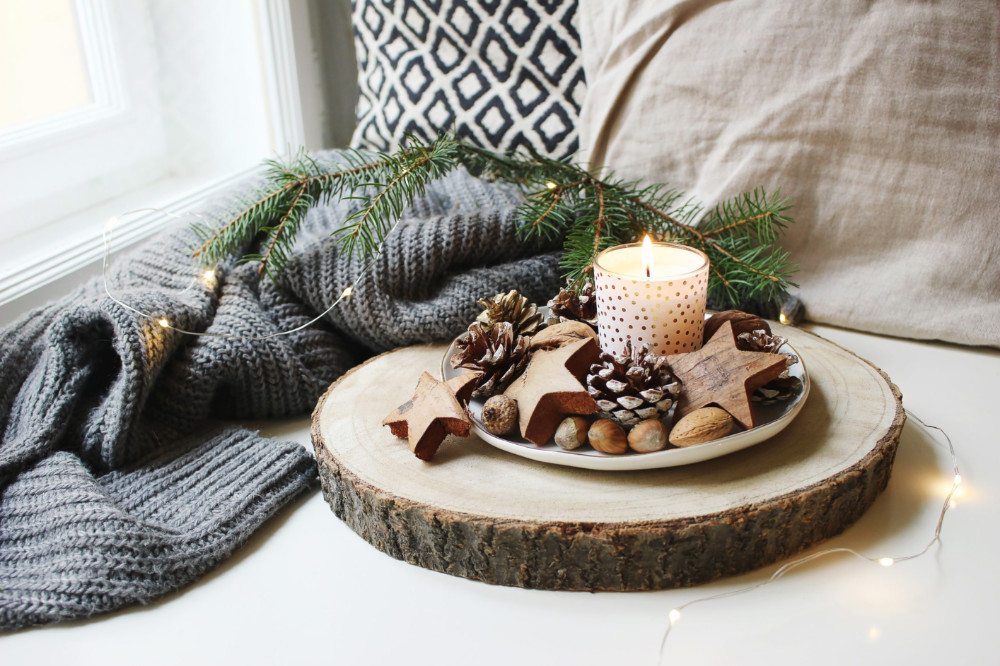 A votive candle on a plate with pinecones and walnuts, on top of a tree trunk slice.
