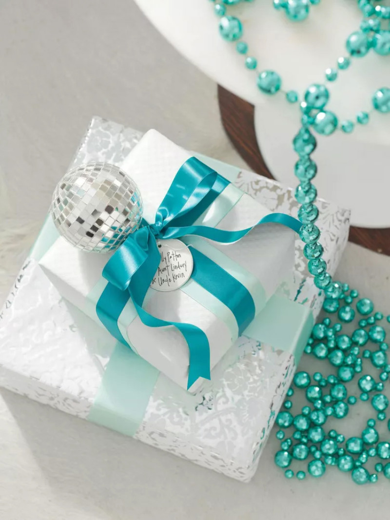 A close-up of two gifts wrapped in white with turquoise ribbons.