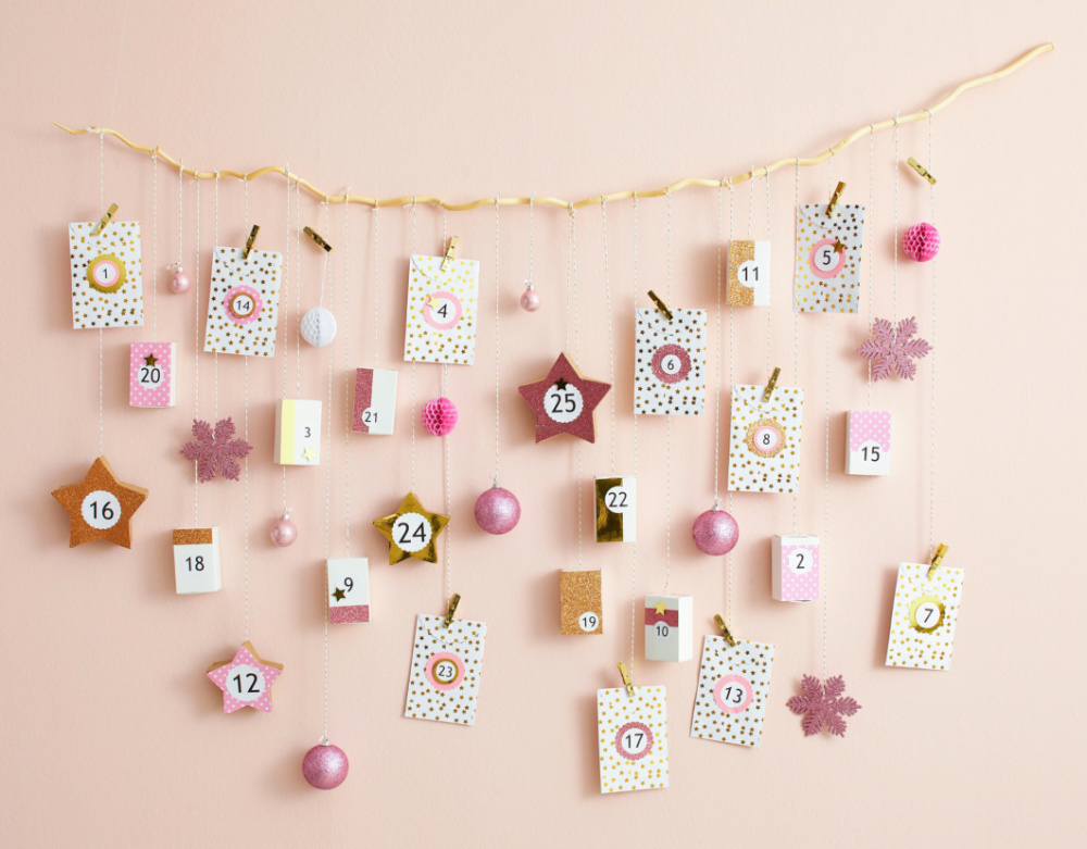 An advent calendar made of postcards of various sizes hanging against a light pink wall.