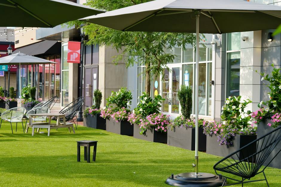 External environment with well-mowed lawn, neatly trimmed foliage, matching chairs, umbrellas, and tables
