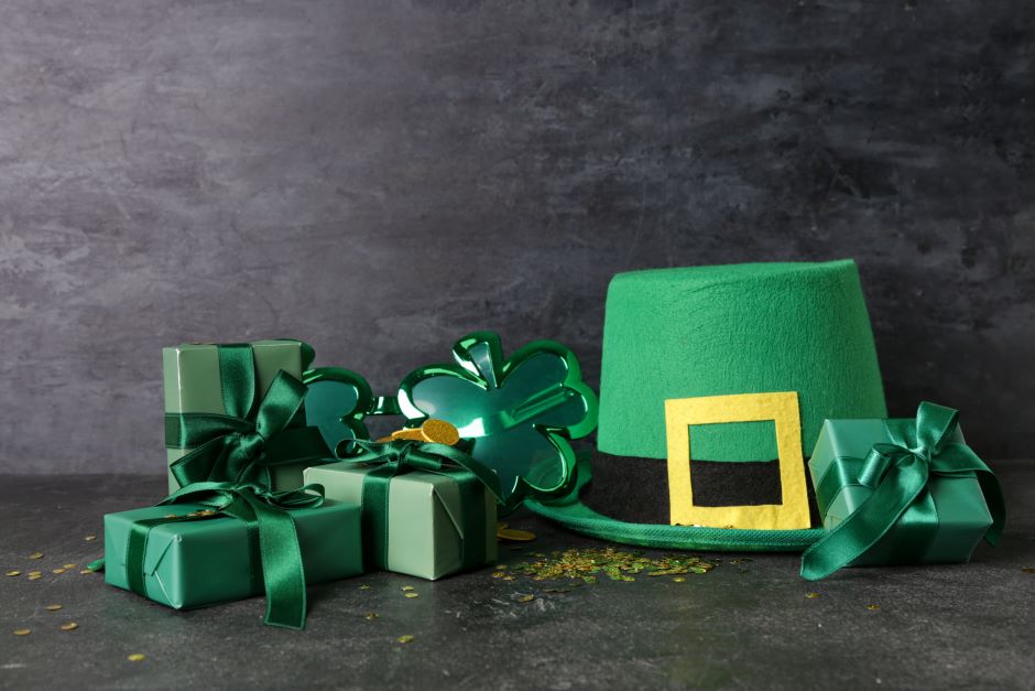 St. patrick's day leprechaun hat with plastic eyeglasses, gift boxes and sequins on black grunge background
