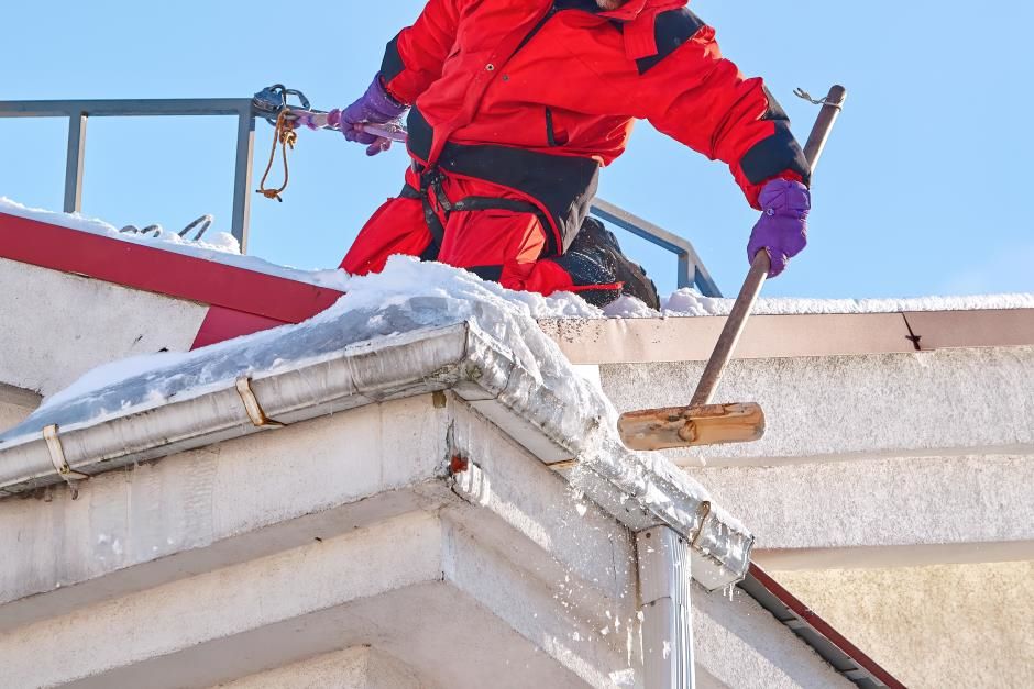  Professional on the roof with safety equipment removing snow from the roof and gutters.