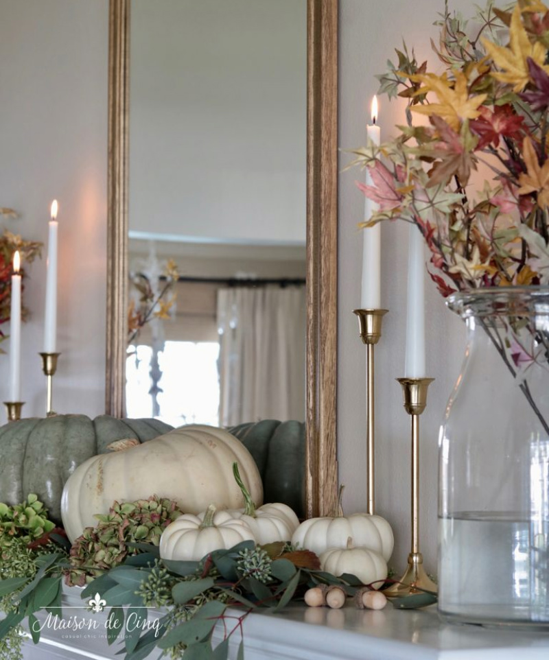 White pumpkins and tall candlesticks in front of a large mirror over the mantle.