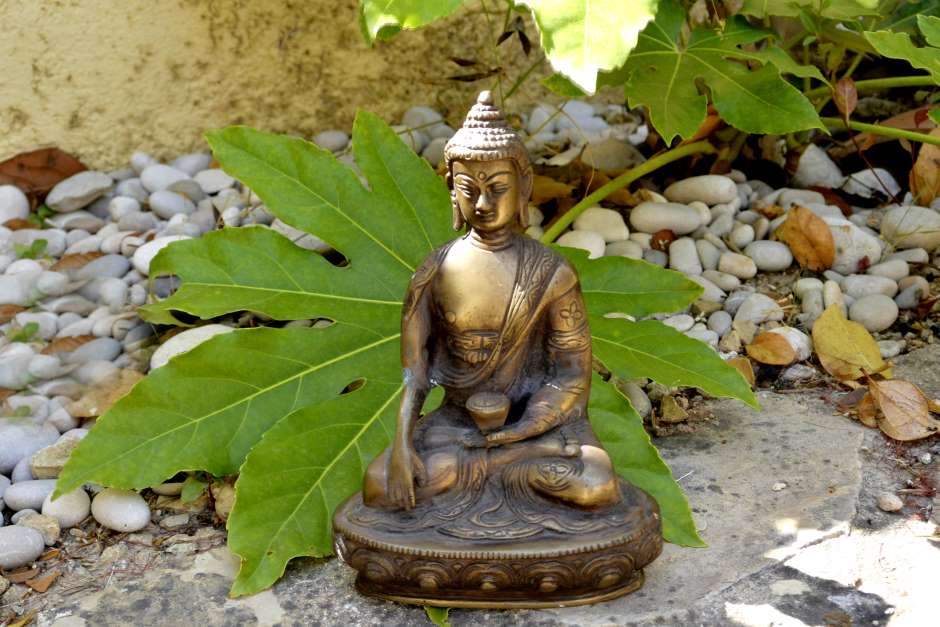 A bronze statue of buddha atop of a stone  in a garden