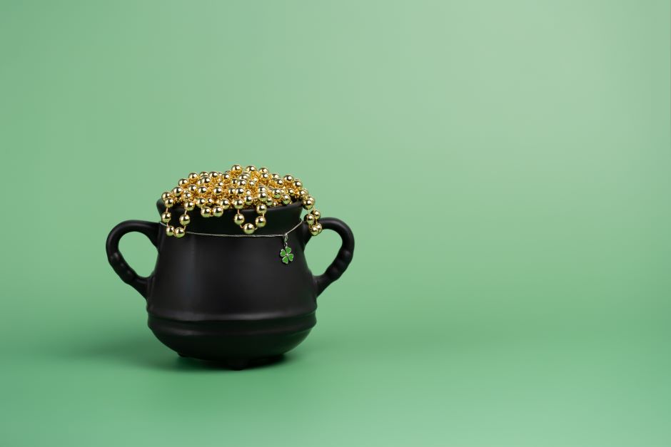 St Patrick's days black cauldron pot with a clover charm and gold beads on green background 
