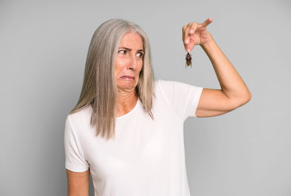 Woman holding a cockroach in her hand, with an expression of disgust on her face