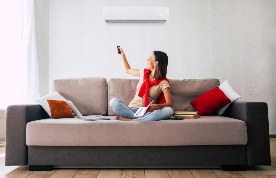 A woman comfortably sitting on her couch turned to her ac with the ac remote