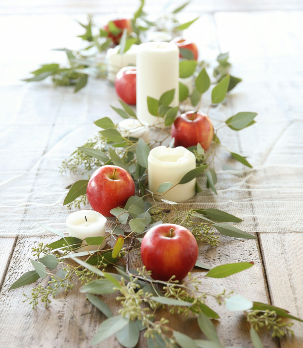 A table runner made of apples, leaves, and votive candles, over a bare wooden table.