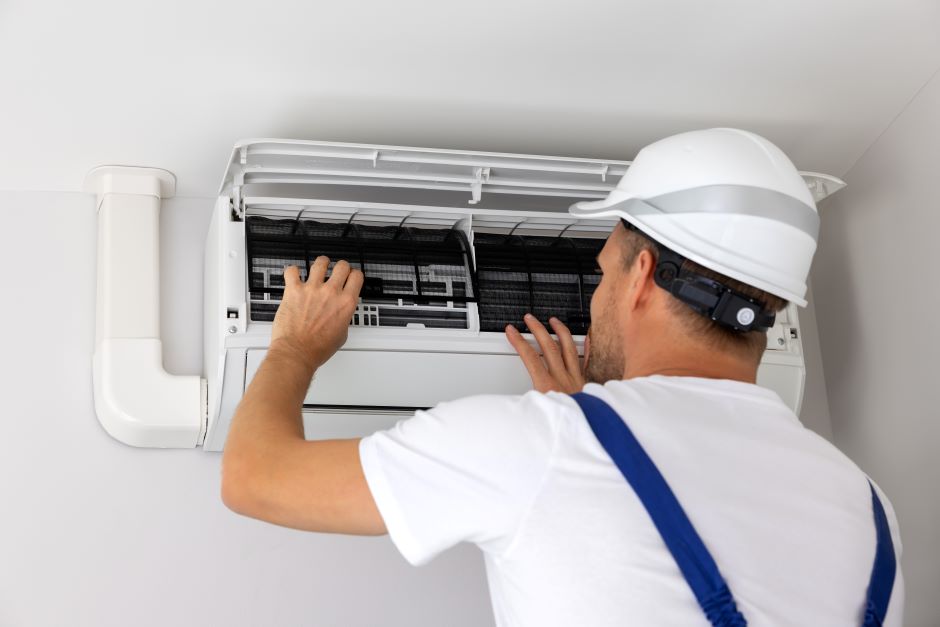 Image of a man fixing an air-conditioner. He is using a safety helmet.