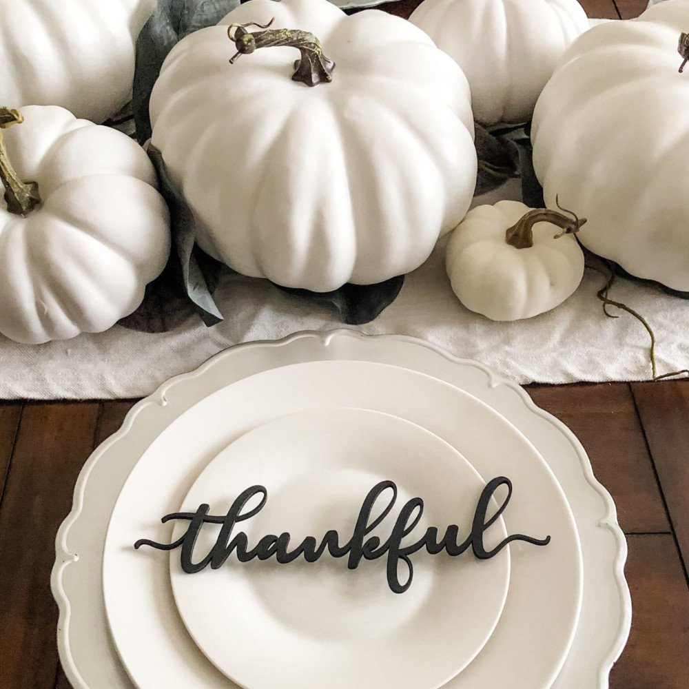 A table runner made of white pumpkins of various sizes, next to a white plate with an ornate “thankful decal.