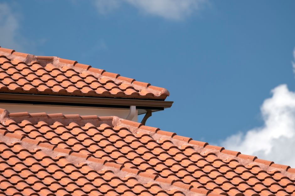 Image showing the roof of a house. The roof tiles are terracotta color. The sky is blue and there are white clouds.