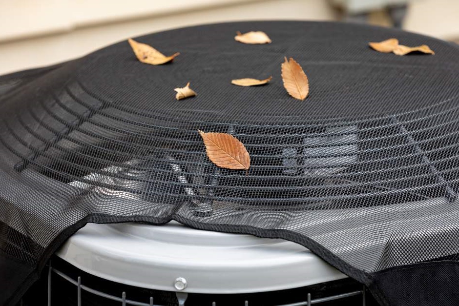 An air conditioning unit with a protective mesh covered with leaves on top