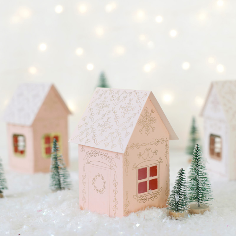 Small DIY paper houses and tiny pine tree props made to resemble a small village covered in snow.