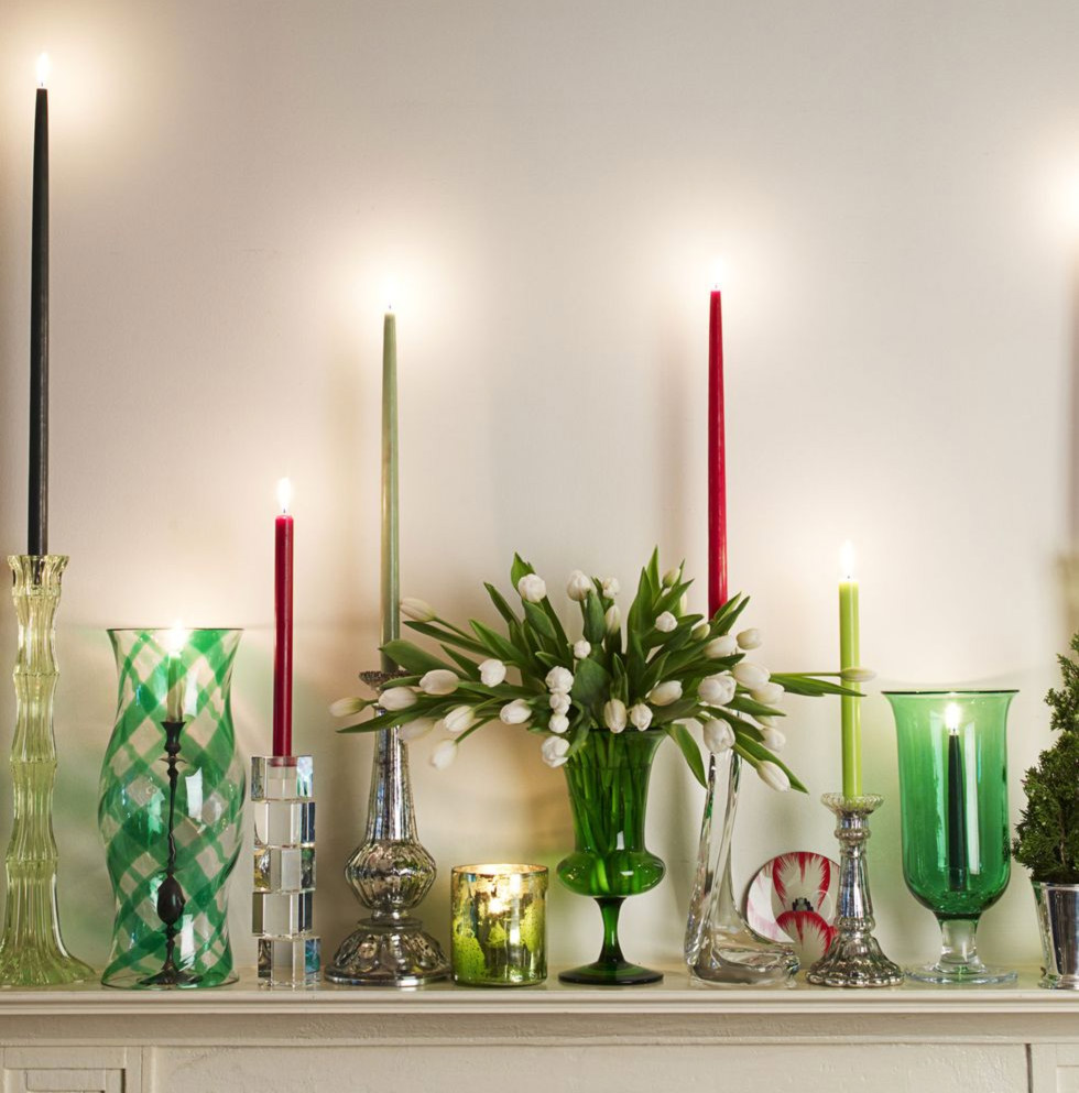 An assortment of tall candles and glass vases over a mantle.