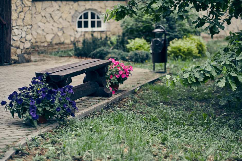 Rustic garden with a wooden bench with a red flower vase on one side and a blue flower vase on the other side standing on sidewalk tile