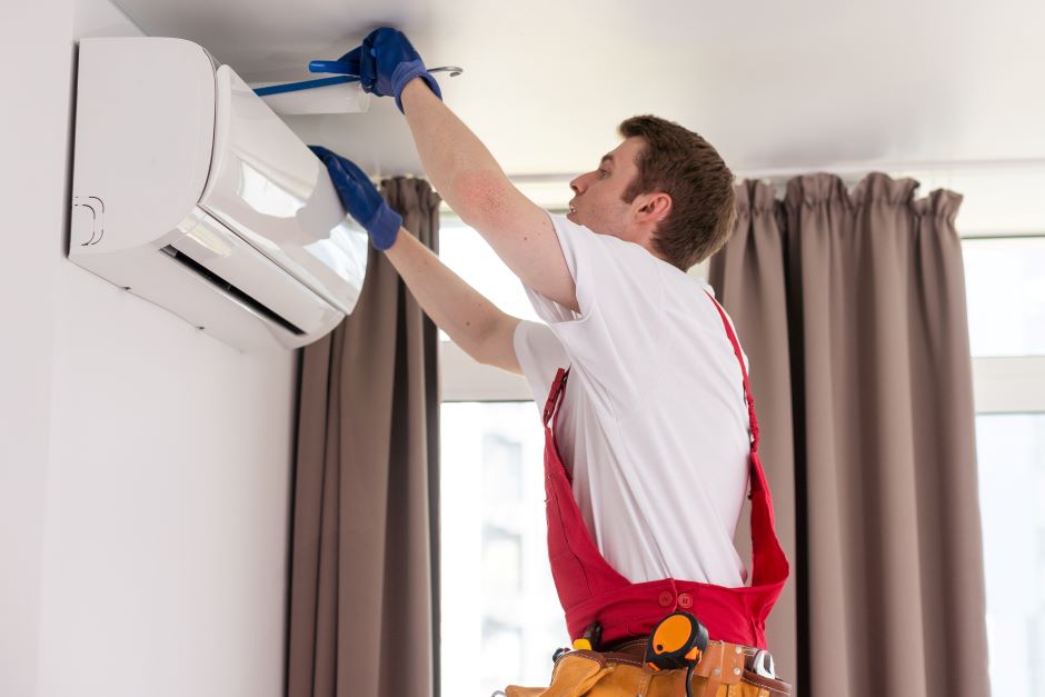 Man using a red jumpsuit and blue gloves trying to repair an air-conditioner